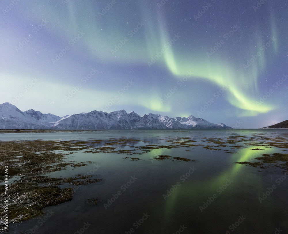 Northern lights is reflected on the icy shore. Spaknesora naturreservat, Djupvik, Lyngenfjord, Lyngen Alps, Troms, Norway, Lapland, Europe. Northern lights is reflected on the icy shore. Spaknesora naturreservat, Djupvik, Lyngenfjord, Lyngen Alps, Troms, Norway, Lapland, Europe.