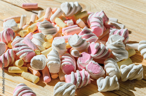 Multicolored marshmallows on bright wooden table. Background of multi-colored and different in shape and size of marshmallows. Sweets background photo