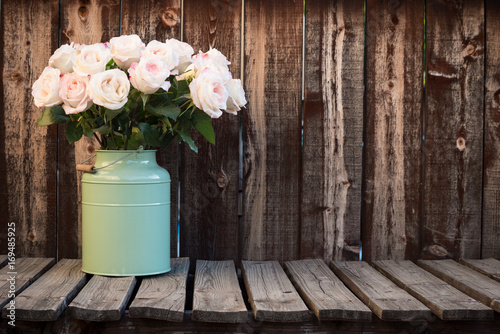 Fototapeta Naklejka Na Ścianę i Meble -  Pink roses in a green bucket style container on a wooden plank table.