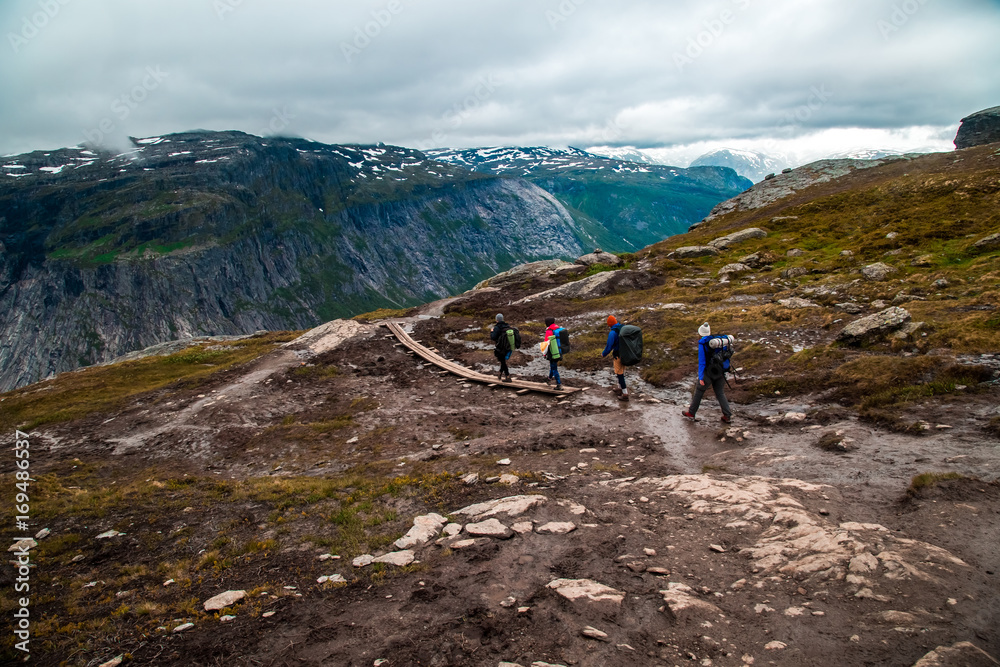 Group of hikers walking in the nature. People hiking with backpacks, tracking in the mountains. People walk the trail to Troll's Tongue (Trolltunga) rock in Hordaland county, Norway. The 22km trail to