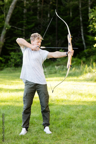 Confident Man Aiming With Bow And Arrow In Forest