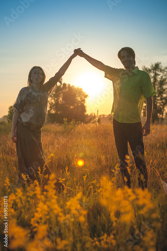 A silhouette of pregnant beautiful woman with her husband on nature landscape smiling and touching hands with love and care. Happy couple, family relax on sunset
