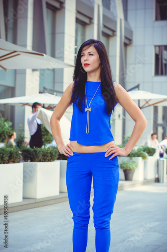 A woman in a blue suit with dark long hair awaits her friends in the city near the restaurant. The lifestyle of a large metropolis and citizens