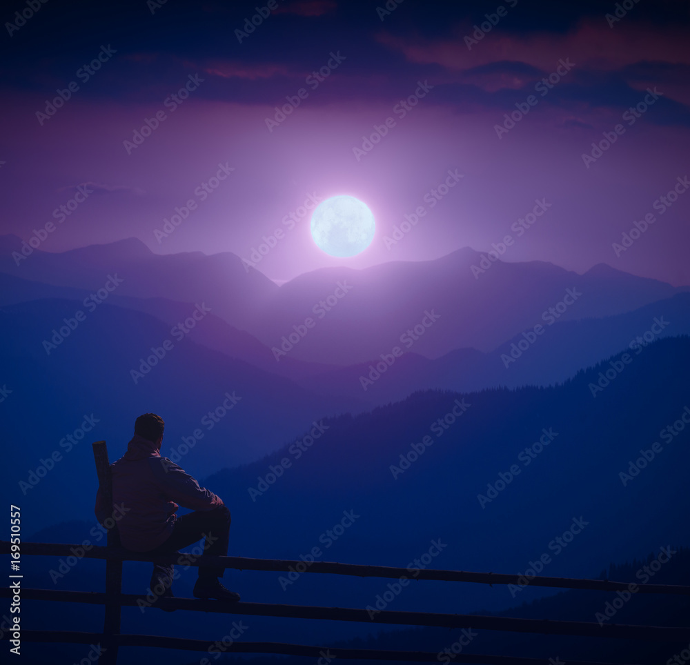 Man sitting on a wooden fence and enjoy full moon rising