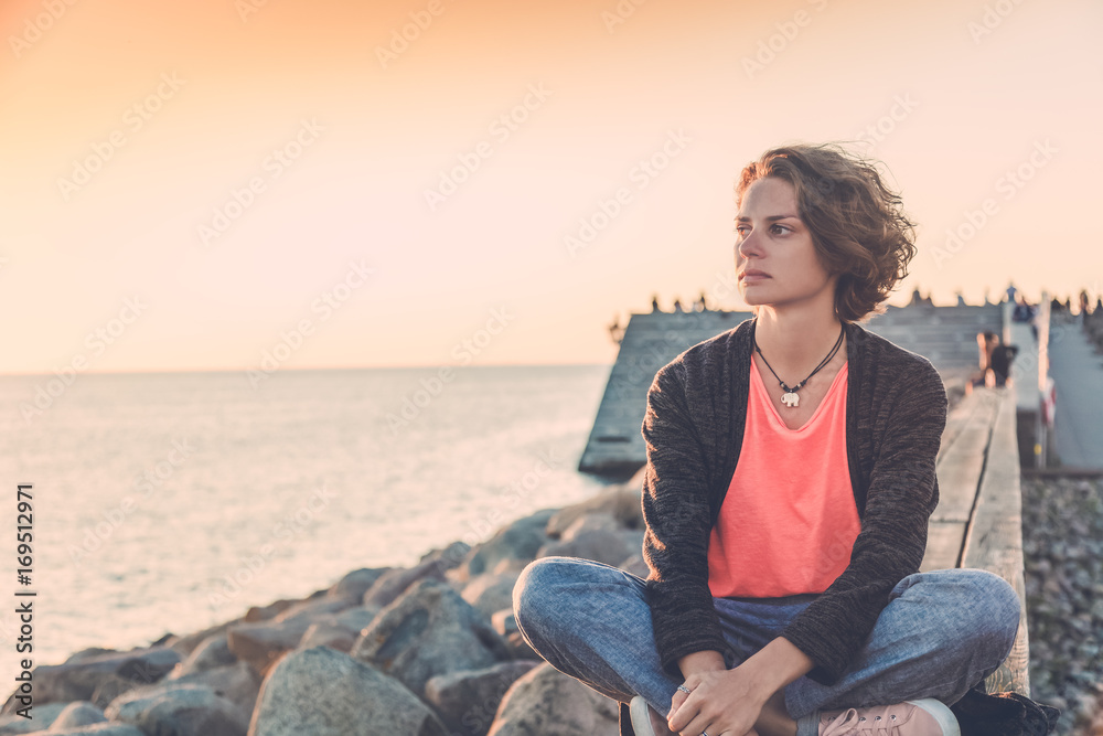 Beautiful young woman sitting on the beach watching the sunset