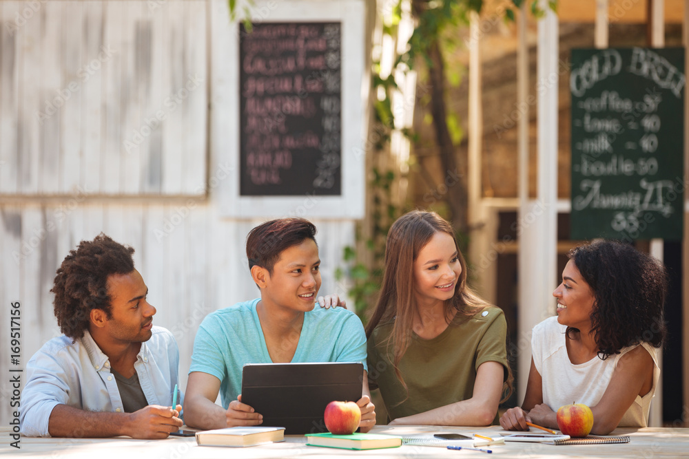 Four young frineds sitting by the table outdoors Four young frineds sitting by the table outdoors