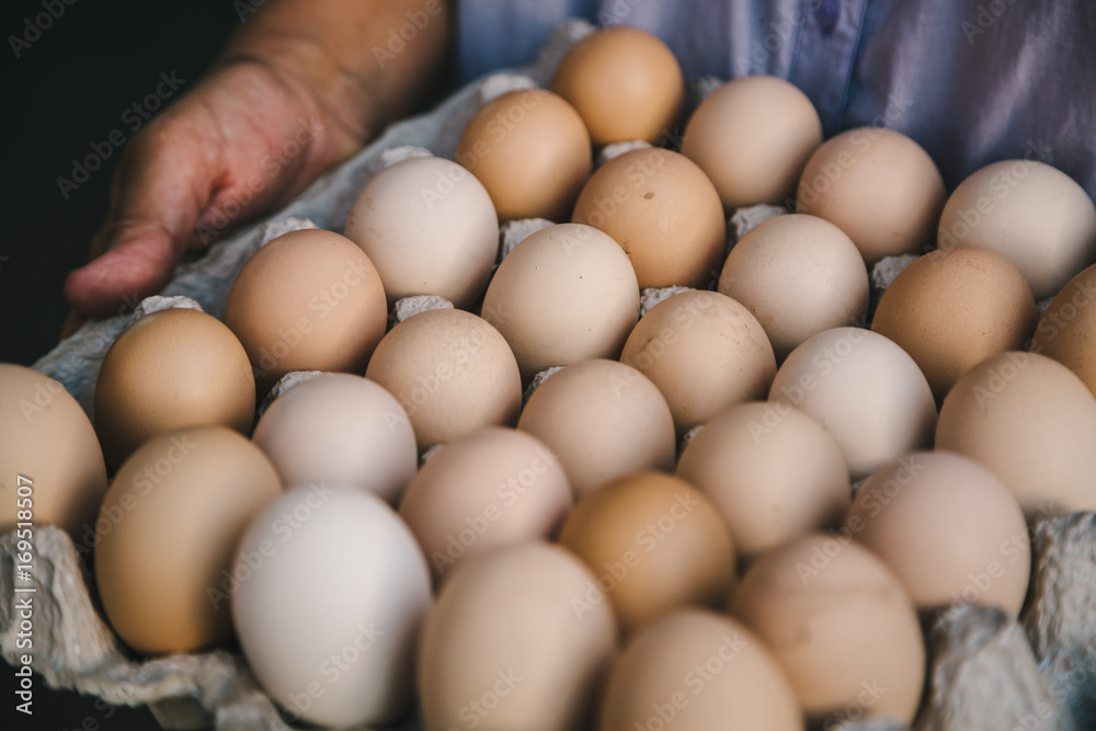 Crop person holding paper carton with dozens of fresh eggs. Crop person holding paper carton with dozens of fresh eggs.