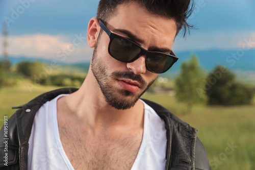 young man in leather jacket and  sunglasses posing outdoor