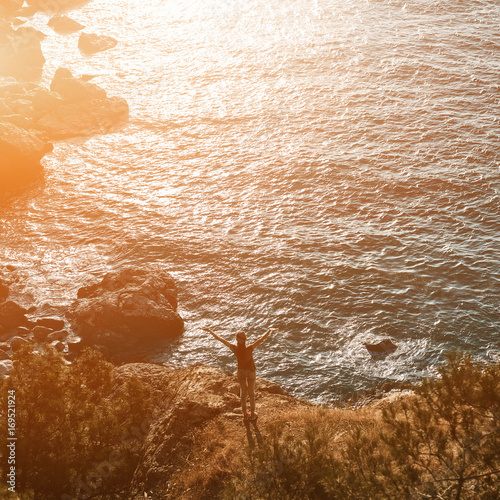 Back view of woman standing on the sea coast Between pines and Enjoying the sunset photo