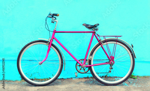 Retro old pink bicycle stands on a colorful blue background
