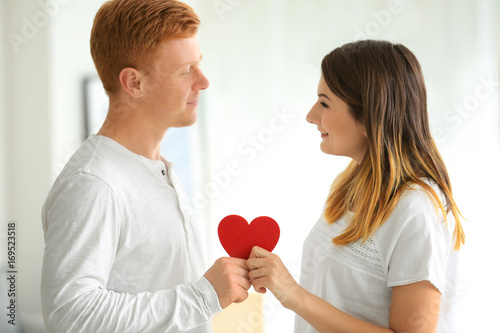 Lovely couple with red heart in light room