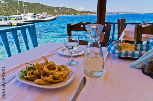 Fried squid and white wine in a shade of a typical greek taverna in a harbour at Amoulani island, Greece