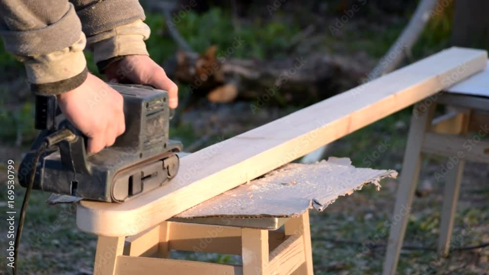 Male hands polishing wooden plank with belt sander outdoors