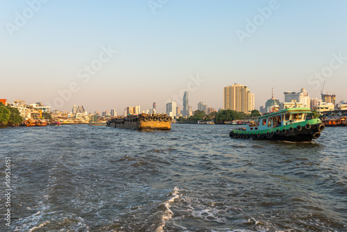 Pusher with barges on the Chao Phraya river in Bangkok. The river meanders through the city in southward direction, emptying into the Gulf of Thailand approx 25 kilometres south of the city centre