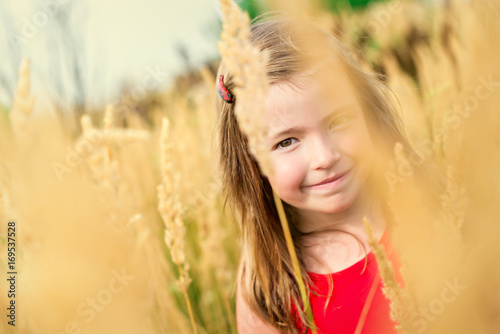 Portrait a happy kid girl among high field grass at summer day