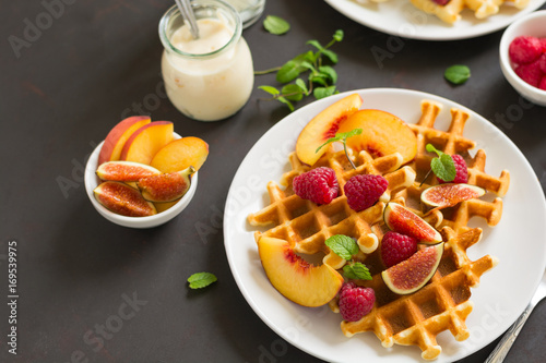 Homemade Belgian waffles with peach, raspberry, fig and honey on brown wooden background. Selective focus