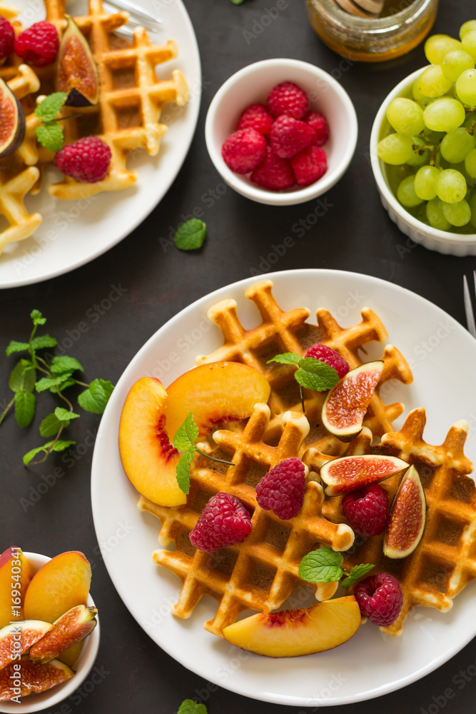 Homemade Belgian waffles with peach, raspberry, fig and honey on brown wooden background. Selective focus Homemade Belgian waffles with peach, raspberry, fig and honey on brown wooden background. Selective focus