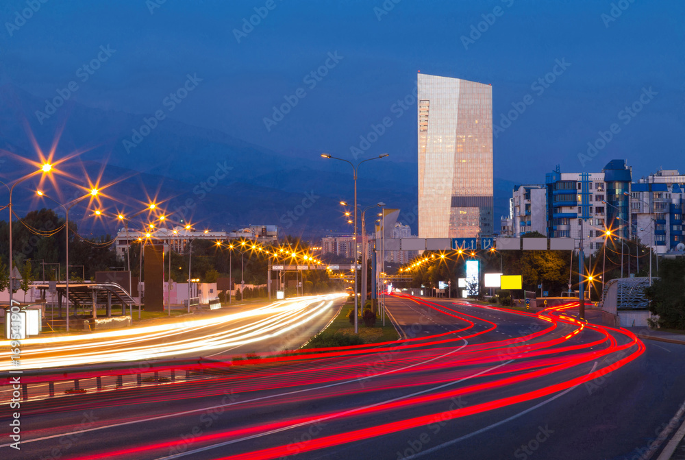 Traffic on a freeway. 
An urban highway early in the morning. Blurry traffic light trails over the road. Distant buildings and mountains are in the background.