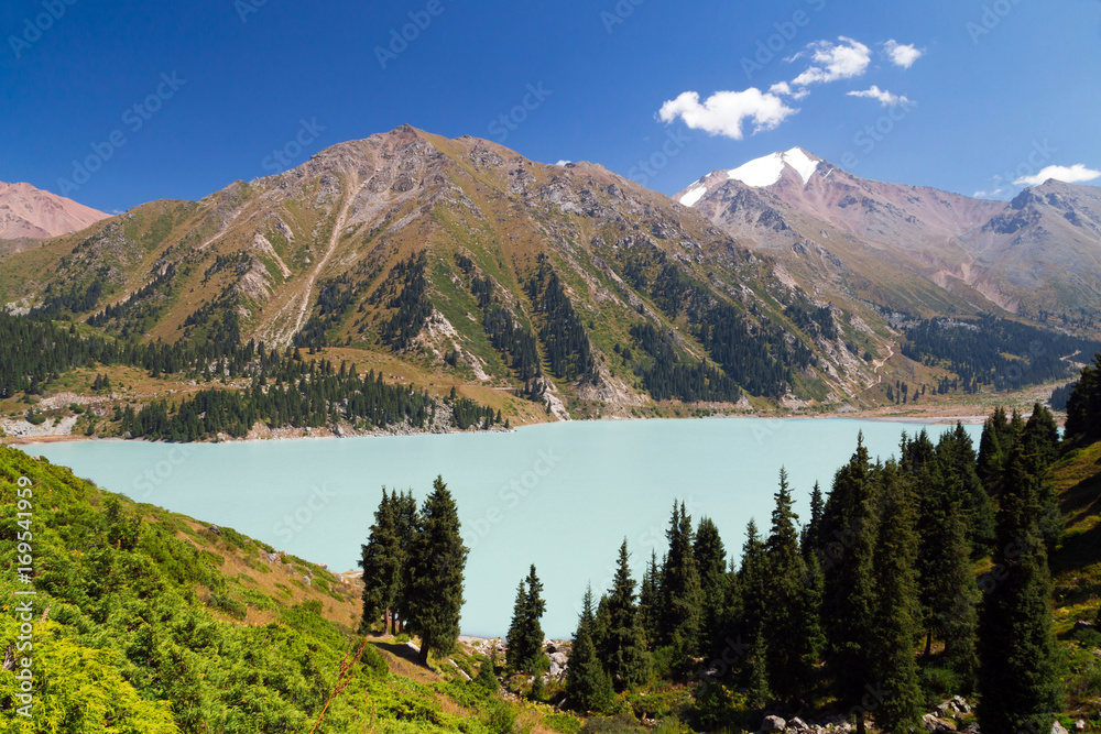 Big Almaty lake. 
View of a lake in the mountains. Snow-capped peak in the background. Sunny summer afternoon.