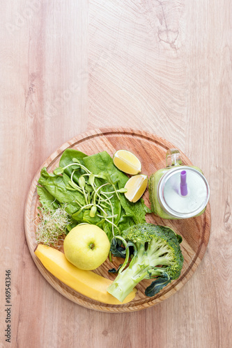 Fresh green vegetables and green smoothie in jar. Detox, diet or healthy food concept. Mason jar of dietary drink with broccoli, spinach, microgreens, lime and banana on wooden background. Top view.