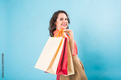 Beautiful young woman holding shopping bags on blue background. Discount, sale, buy and shopaholic concept