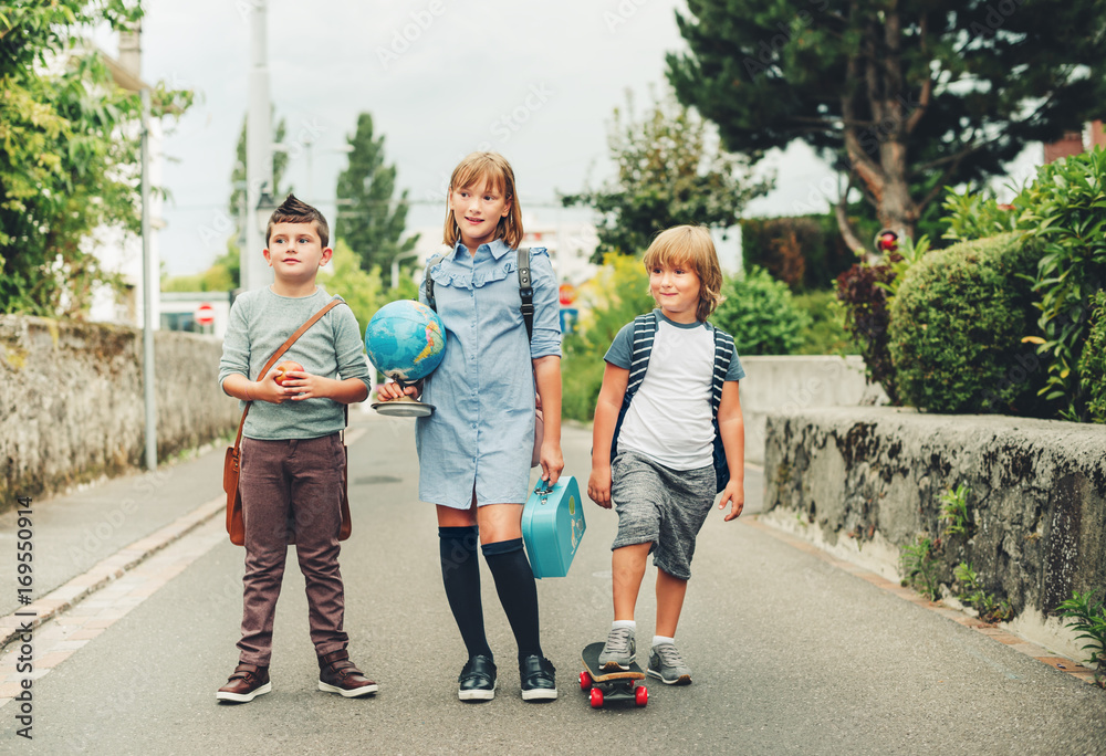 Group of three funny kids wearing backpacks walking back to school. Girl and boys enjoying school activities. Globe, lunch box, red apple and skateboard accessories. Group of three funny kids wearing backpacks walking back to school. Girl and boys enjoying school activities. Globe, lunch box, red apple and skateboard accessories.