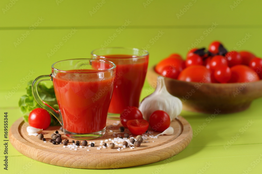 Fresh tomato juice in glass mugs. Mugs of tomato juice and fresh tomatoes on a green wooden background. Fresh tomato juice in glass mugs. Mugs of tomato juice and fresh tomatoes on a green wooden background.