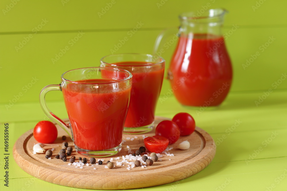 Fresh tomato juice in a glassware. Mugs of tomato juice and fresh tomatoes on a green wooden background. Fresh tomato juice in a glassware. Mugs of tomato juice and fresh tomatoes on a green wooden background.
