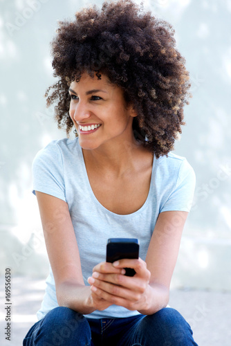 Happy woman with curly hair holding smart phone