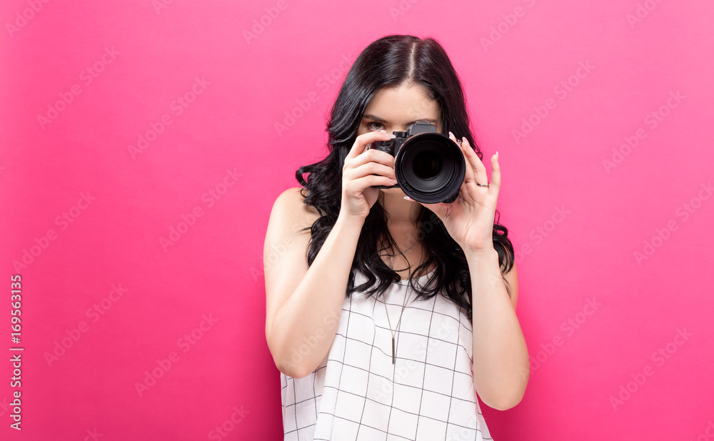 Young woman holding a camera on a pink background Young woman holding a camera on a pink background