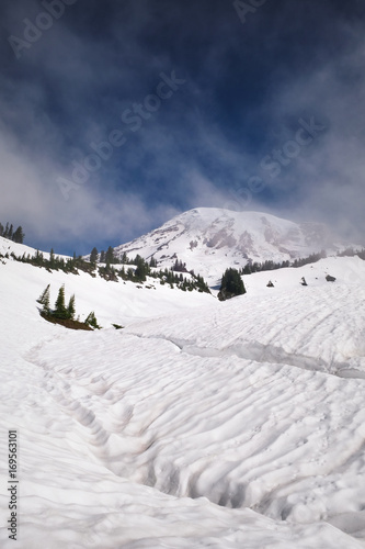 Mount Rainier with a snow-covered lake in the foreground during June