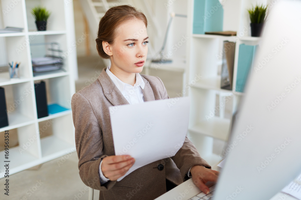 Young accountant with paper sitting in front of pc monitor in office Young accountant with paper sitting in front of pc monitor in office