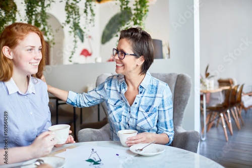 Happy employer lauding happy young subordinate by cup of coffee in cafe