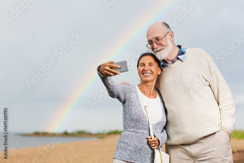 Contemporary seniors making selfie at summer resort