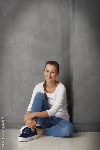 She is so lovely.Full length studio portrait of a cute young woman sitting at grey wall with copy space. 