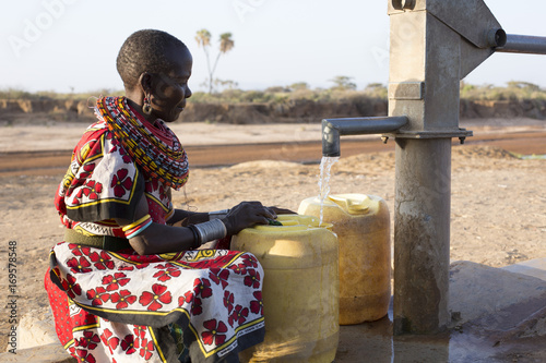 Samburu tribal woman collecting fresh water from borehole  in desert landscape. Kenya, Africa. photo