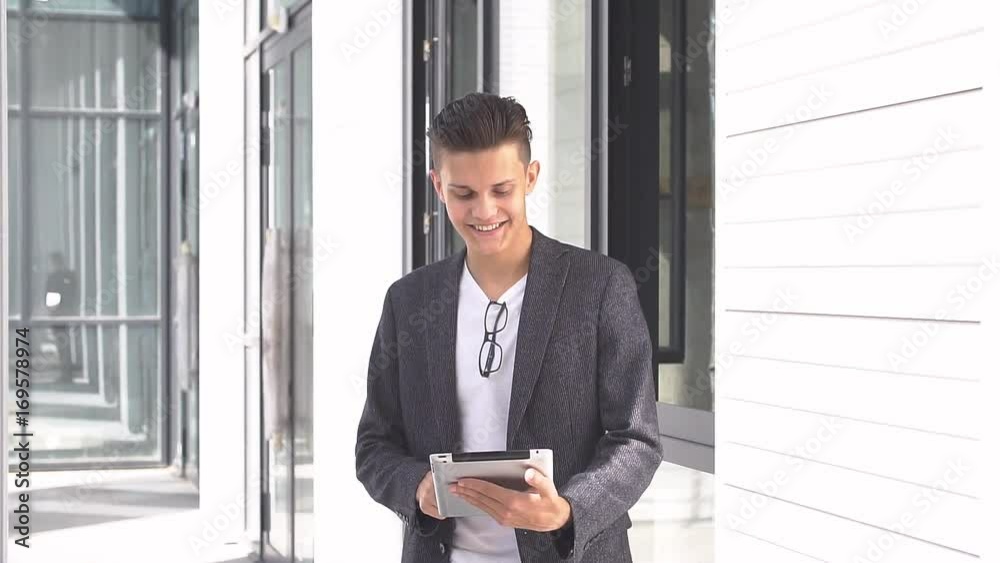 Young businessman uses tablet on background of modern building. Young businessman uses tablet on background of modern building.