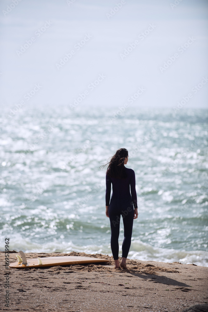 Surfer silhouette of a woman wearing wet suit looks at the sea Surfer silhouette of a woman wearing wet suit looks at the sea