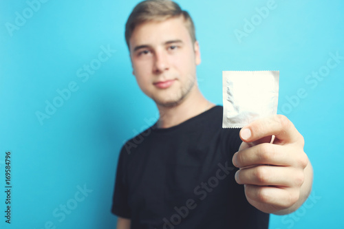 The guy is holding a condom on a blue background.