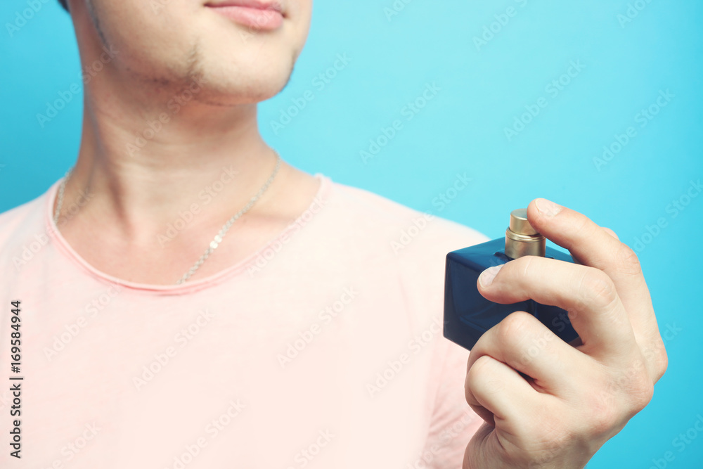 Fototapeta premium The guy holds a bottle of perfume on a blue background in his hand.