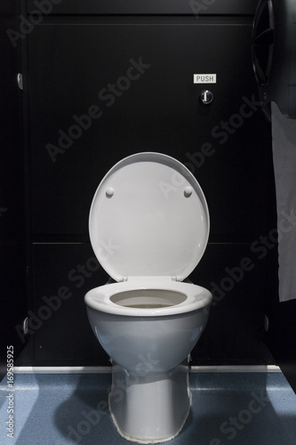 White porcelain toilet with lid up in a black stall