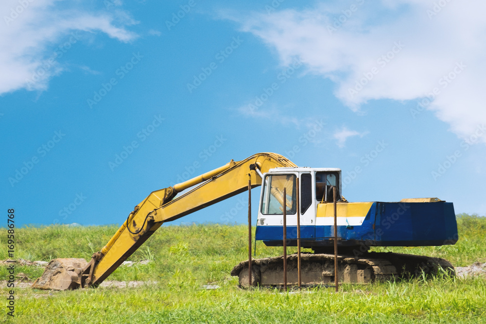 Backhoe is working at grass field on blue sky background Backhoe is working at grass field on blue sky background