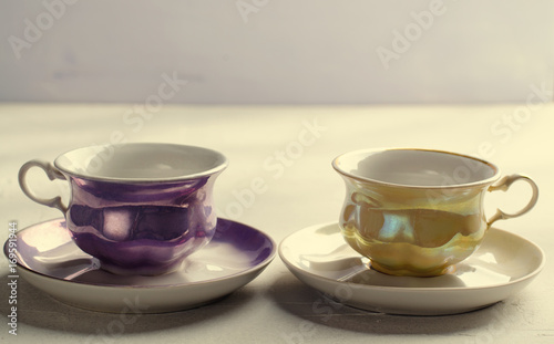Empty colorful porcelain tableware. Yellow and violet cups on lilac background. Toned