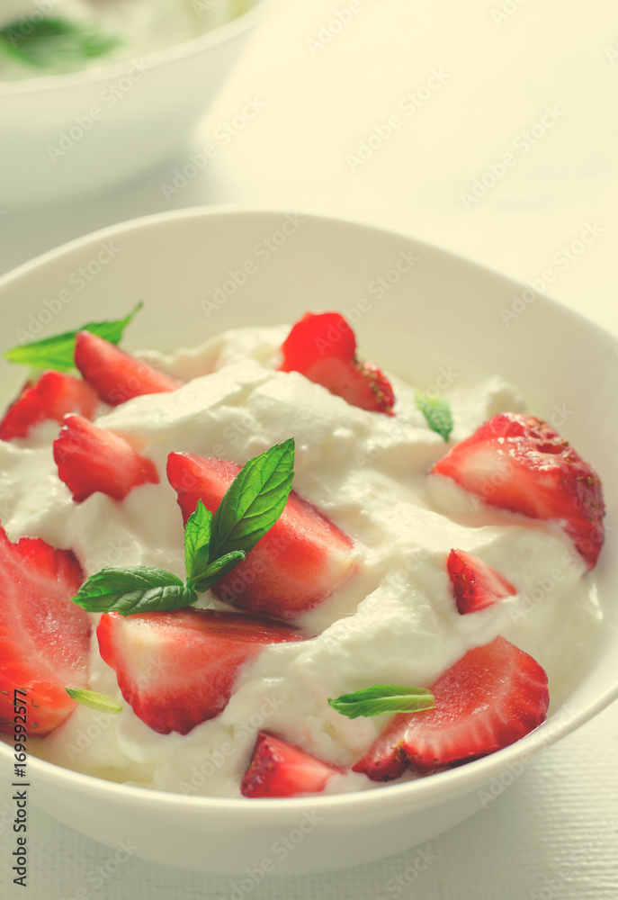 Breakfast with bowl of thick organic greek yogurt and fresh strawberries on white backgfound. Toned