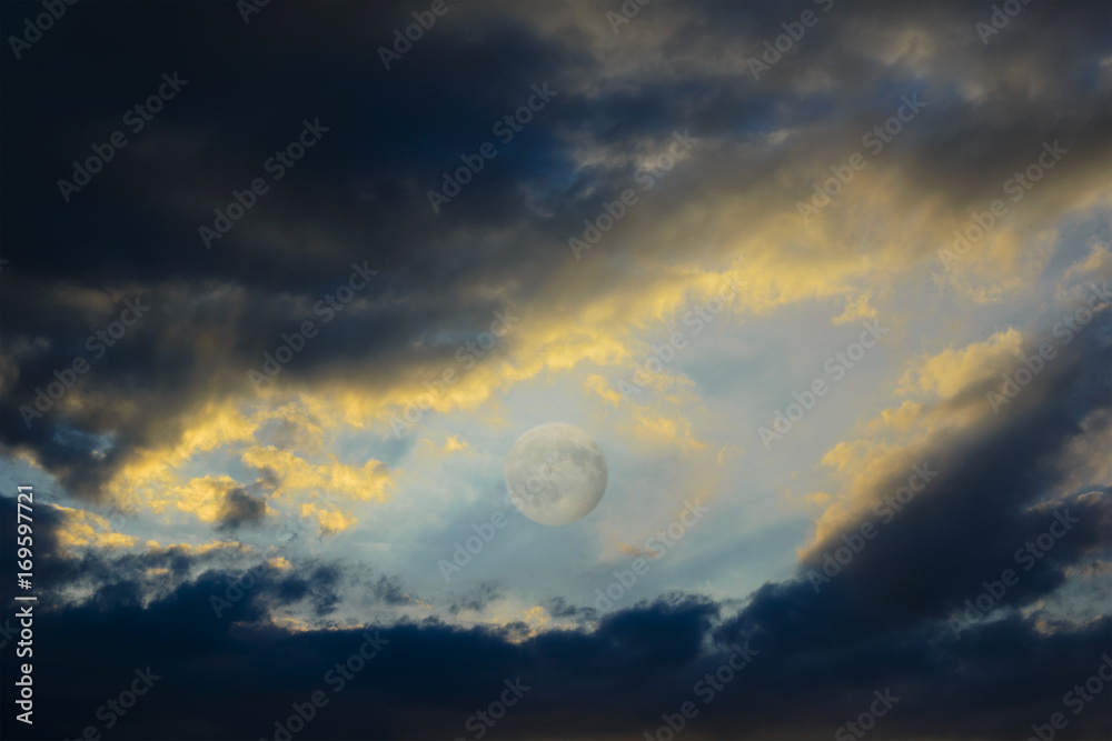 Between the dark clouds backlit by the sunset there is the full moon Between the dark clouds backlit by the sunset there is the full moon