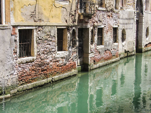 Canal with bright green water against old building with exposed bricks in Venice, Italy