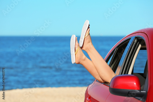 Legs of beautiful young woman relaxing in car at sea shore