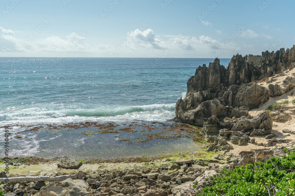 A rocky beach with green shrubs, breaking waves and interesting stone formations above, along the Heritage Trail, on Kauai A rocky beach with green shrubs, breaking waves and interesting stone formations above, along the Heritage Trail, on Kauai