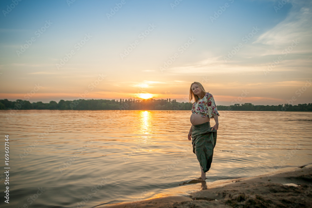 A pregnant beautiful woman on the river bank beach smiling with her mehandi ornament belly with love and care. Happy woman on sunset