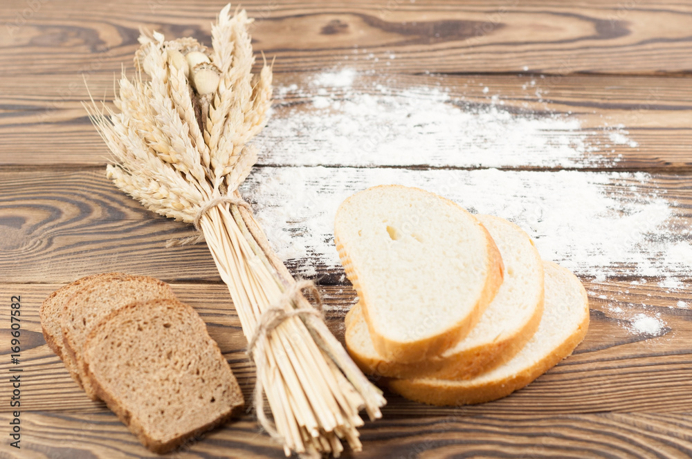 One bundle of wheat and poppy and strewn flour and slices of bread on old rustic wooden planks One bundle of wheat and poppy and strewn flour and slices of bread on old rustic wooden planks